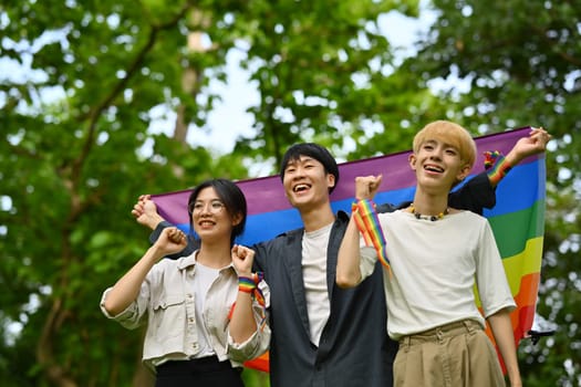 Happy young LGBT friends with rainbow heart celebrating gay pride, enjoying outdoor activities at outdoor.