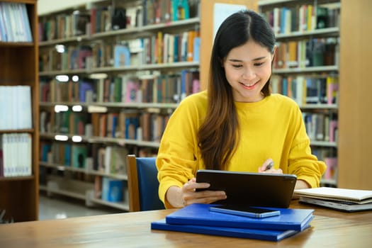 Smiling female college students preparing for exam, searching information on digital tablet in library.