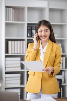 Young busy asian business woman talking on phone working in modern office. Asian businesswoman company sales client manager wearing suit making call on cellphone sitting at workplace...