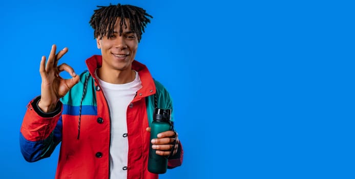 Positive african man makes OK hand sign, okay gesture. Happy student guy, correct perfect choice, great deal, blue studio background. Water battle. High quality photo