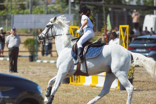 Equestrian sport - a little girl in white uniform competing on a horseback at the ranch. Mid shot