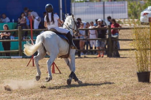 Equestrian sport - a girl in uniform riding white horse at the ranch. Mid shot