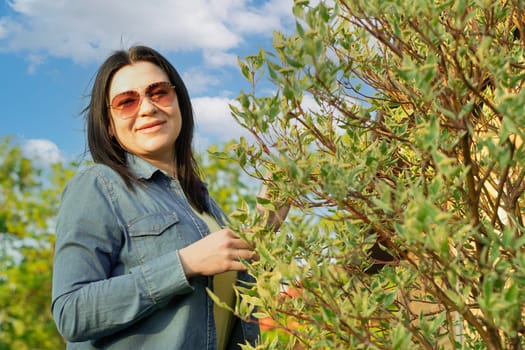 Camping. A beautiful girl in jeans and sunglasses, stands near a blooming green tree, smiles happily. Fresh air concept. Sunset.