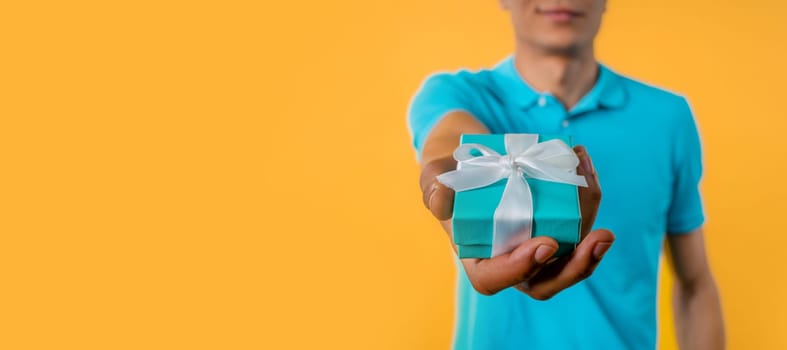 Man gives gift box by hands to camera, yellow background. Present, offer surprise for you. High quality photo
