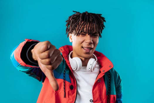 Portrait of unhappy man condemns with sign of dislike. Young millennial guy expressing discontent with showing thumbs-down gesture on blue studio background.