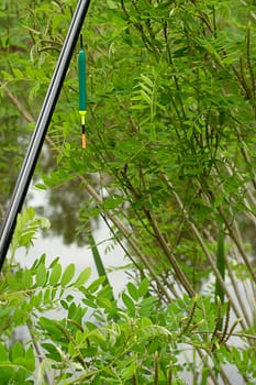 Fishing concept. A fishing rod with a float on the background of green trees and a lake. Catching fish in spring. Fresh air