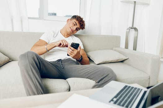 man interior cellphone couch online young modern business student blogger phone mockup lifestyle mobile teenager curly holding laptop blissful