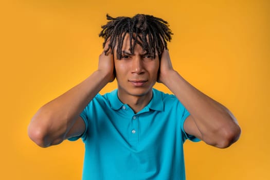 Irritated african man with covered ears ignoring on yellow background. Teenager banning annoying sounds, shouts or noise. High quality
