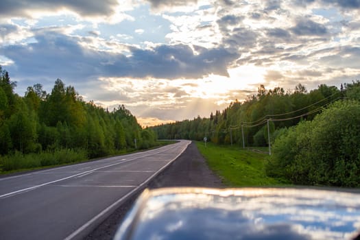 Country road with markings in the middle of the forest. Path and forward movement in the sun. Beautiful, green forest in the spring at sunset. Concept for success in the future goal and passing time