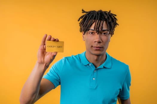 Successful handsome african american man showing unlimited gold credit card and look to camera yellow studio background. High quality photo