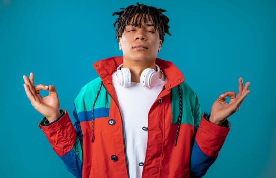 Calm man relaxing, meditating, refuses stress. Dreadlocks haired guy breathes deeply, calms down blue studio background. Yoga, moral balance, zen concept. High quality