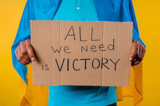 Ukrainian man with cardboard All we need is victory on yellow background. Ukraine will win war. Democracy, liberty, demonstration, russian aggresion concept. High quality photo