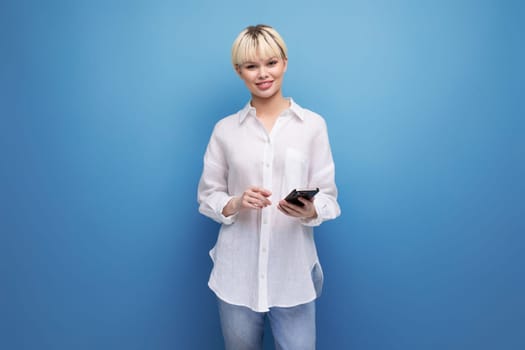 young cheerful pretty blonde businesswoman in a white shirt holds a phone in her hand against the background with copy space.