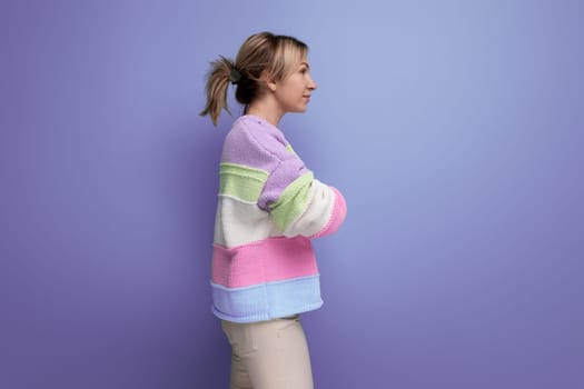 cute shy blond young woman standing in profile on purple background with copy space.