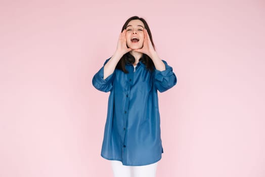 Portrait of young woman with joyous expression, hands near open mouth as if sharing news or telling a funny story, beaming a big toothy smile, isolated on bright pink background