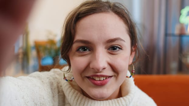 POV of young woman making online selfie video call talking waving hand hello, looking at camera at home apartment indoors. Communication, meeting. Brunette girl blogger making smartphone conversation