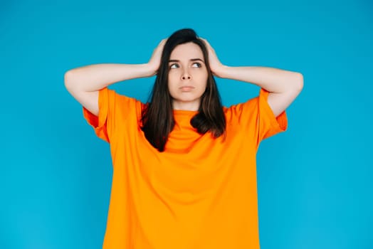 Stressed Young Woman Expressing Discontent, Touching Head - Negative Emotions, Frustration, Isolated Blue Background.