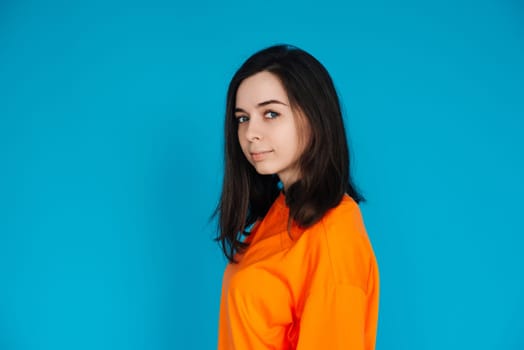 Stunning Young Woman in Trendy Orange Outfit Poses for Portrait, Isolated on Blue Background, Lovely Model with a Captivating Gaze and Gorgeous Appearance.