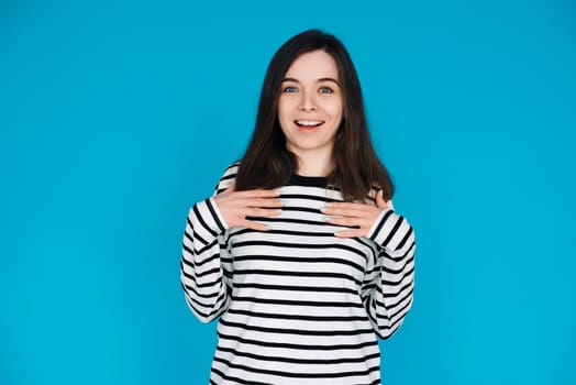 Portrait of a gorgeous, pretty, imposing girl in a striped pullover with her arms across her chest, isolated on a blue background.