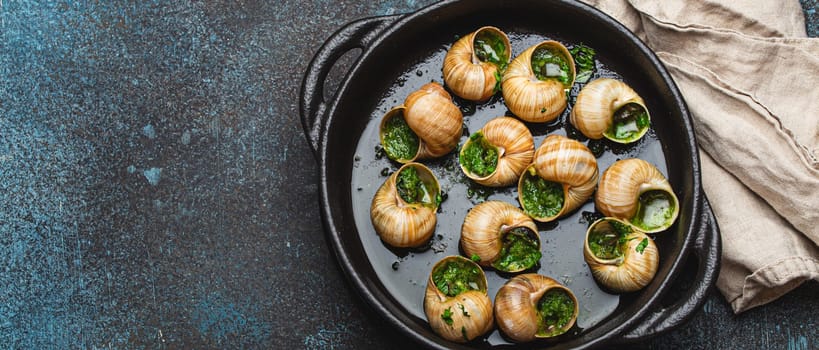 Escargots de Bourgogne Snails with Garlic Butter and Parsley in black cast iron pan on rustic stone background top view, traditional French Delicacy, space for text.