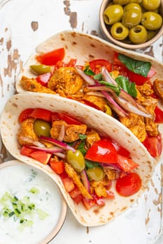 Traditional Greek Dish Gyros: Pita bread Wraps with vegetables, meat, herbs, olives on rustic wooden cutting board with Tzatziki sauce, olive oil top view, white wooden background, closeup.