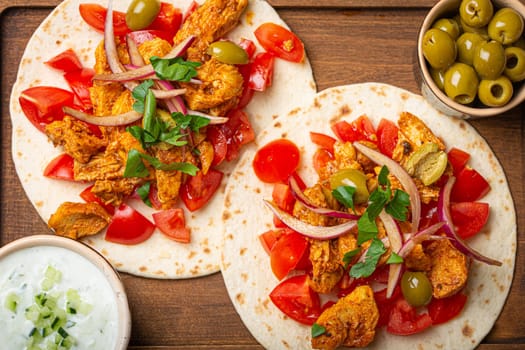 Cooking Traditional Greek Dish Gyros: Closeup of Pita bread with vegetables, meat, herbs, olives on rustic wooden cutting board with Tzatziki sauce, olive oil from above .