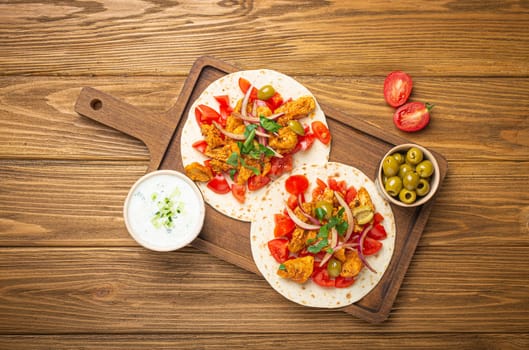 Cooking Traditional Greek Dish Gyros: Pita bread with vegetables, meat, herbs, olives on rustic wooden cutting board with Tzatziki sauce, olive oil top view, wooden light brown background.