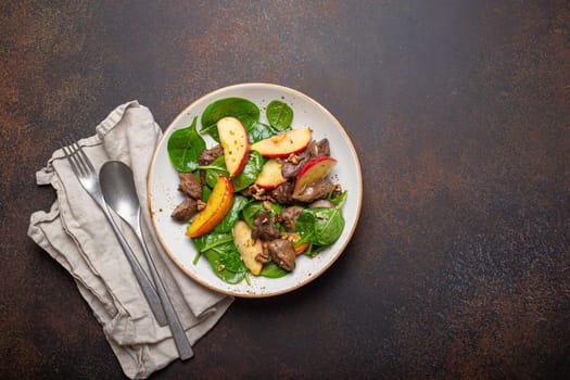 Healthy Salad with Iron Rich Ingredients Chicken Liver, Apples, Fresh Spinach and Walnuts on White Ceramic Plate, Dark Brown Rustic Stone Background Top View Copy Space.