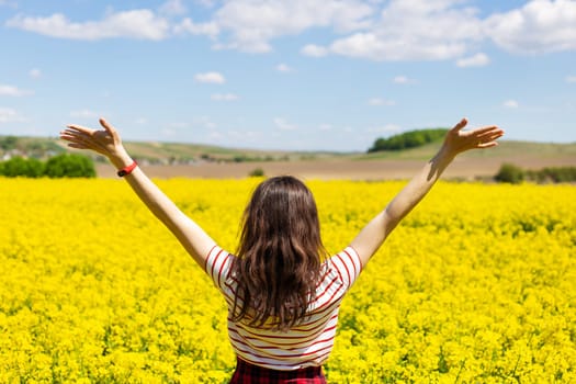 A girl stands in the middle of a beautiful rapeseed field with a beautiful blue sky. Biofuel concept