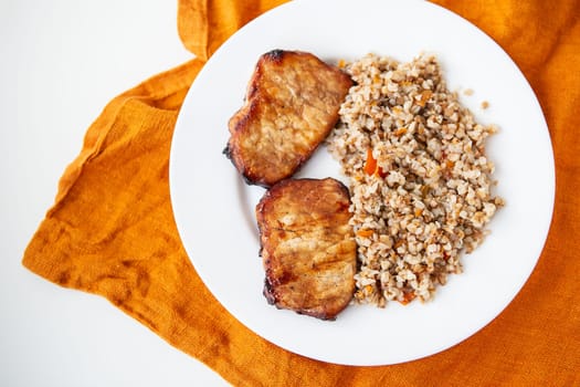 Delicious and appetizing pork tenderloin steak, grilled with buckwheat and vegetables, is on the table along with an orange napkin
