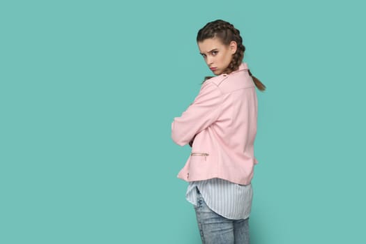 Portrait of upset teenager girl with braids wearing pink jacket turning to camera with sad look, looking at camera, expressing sorrow and sadness. Indoor studio shot isolated on green background.