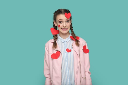 Oops. Portrait of surprised teenager girl with braids wearing pink jacket looking wondered at camera, has amazed expression, clenched teeth. Indoor studio shot isolated on green background.