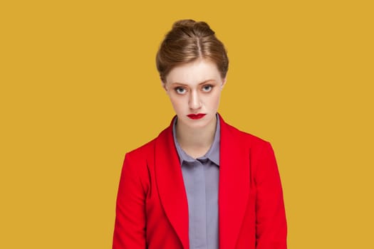 Portrait of unamused sad miserable woman with red lips sulks troubled as someone hurt his feelings, looking at camera, wearing red jacket. Indoor studio shot isolated on yellow background.