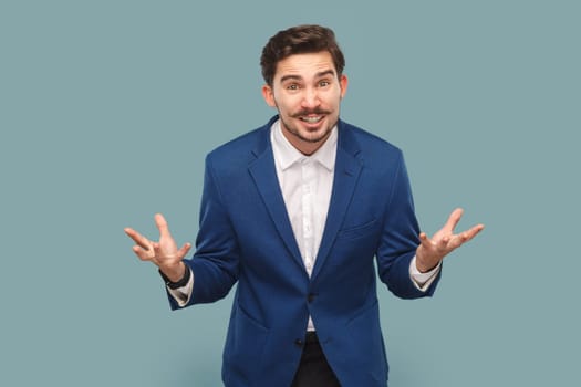 Portrait of aggressive attractive man with mustache standing with clenched hands, yelling with hate and anger, wearing official style suit. Indoor studio shot isolated on light blue background.