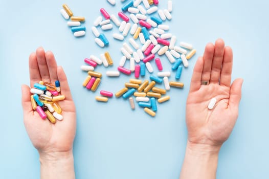 The girl holds a handful of bright vitamins in her hands, and one pill in the other, food supplements and medicines on a blue background. Concept of medicine and healthcare