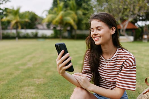 woman blogger happy smartphone network park call shirt cellphone mobile grass smiling female striped outside nature tree lifestyle walk phone palm caucasian