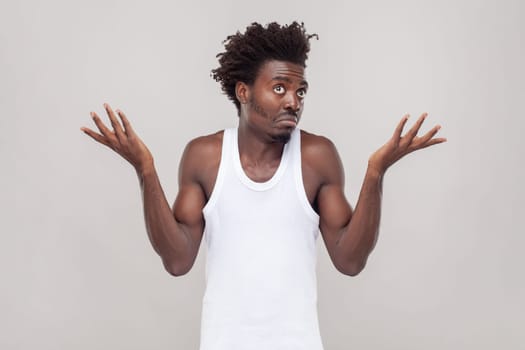 I dont know this. Portrait of confused puzzled man with Afro hairstyle feels uncertain as cant find right way, wearing white T-shirt. Indoor studio shot isolated on gray background.