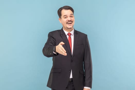 Portrait of friendly positive optimistic man with mustache standing outstretching hand, nice to meet you, wearing black suit with red tie. Indoor studio shot isolated on light blue background.