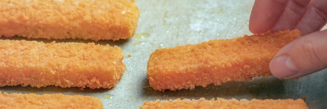The hand puts a lot of fish fingers ready for frying on frying paper. The concept of cooking frying fish sticks in the oven, pan or grill. Close-up. High quality photo