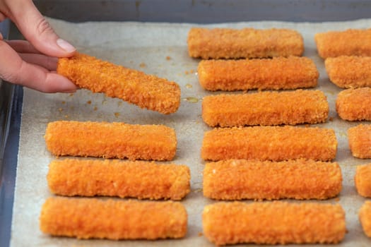 The hand lays out the fish fingers on the frying paper. The concept of frying fish sticks in the oven. Side view. High quality photo