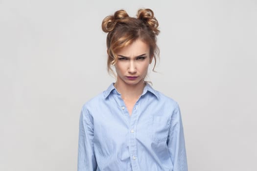 Portrait of annoyed irritated angry blonde woman feeling anxious and nervous, expressing fury and madness, wearing blue shirt. Indoor studio shot isolated on gray background.