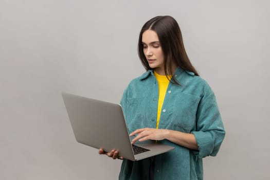 Portrait of smiling freelance worker woman holding laptop, using computer for education or online job, browsing internet, wearing casual style jacket. Indoor studio shot isolated on gray background.