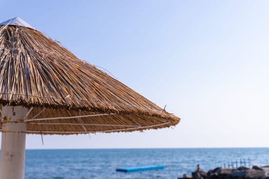 Looking at the blue sea through a straw beach umbrella