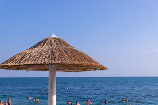 Looking at the blue sea through a straw beach umbrella