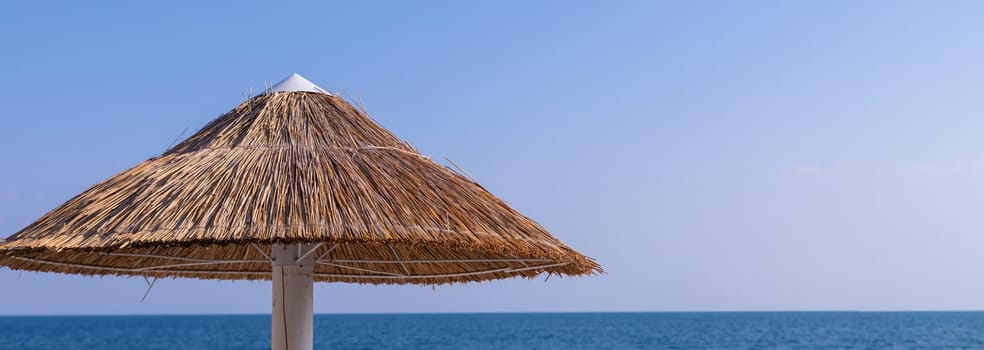 Looking at the blue sea through a straw beach umbrella