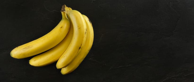 Top view, bunch of bananas on black stone board. Banner with copy space for text on right.