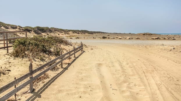 Tire and foot prints on a road leading to beach covered in sand. Sea in distant background.