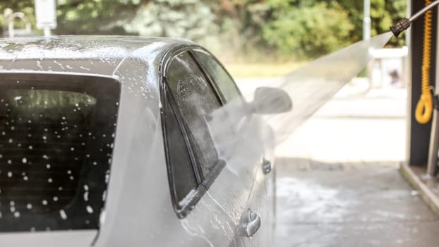 Side of silver car washed in self serve carwash. Water jet stream spraying in air.