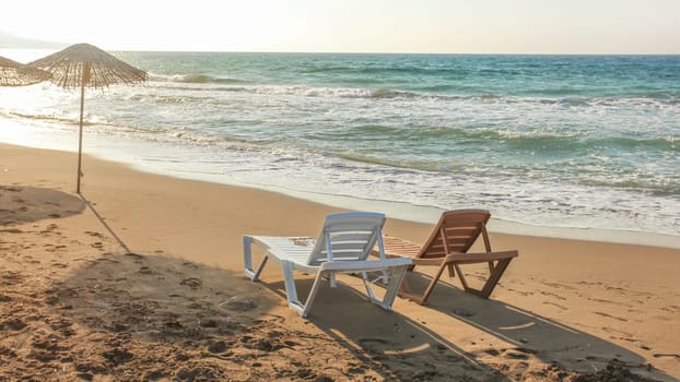 Two empty plastic sunbeds facing the sunset, sea in background. Image illustrating tropical vacation.