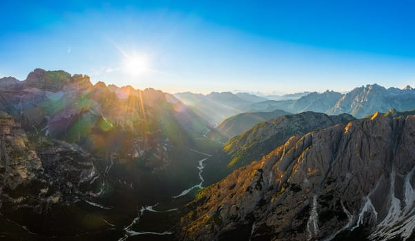 Sharp faces of high mountains at sunrise. Illuminated by sun rays rocky peaks of Tre Cime di Lavaredo under clear sky aerial view in back lit